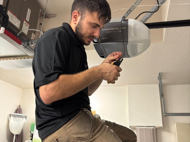 Technician checking a hinge and roller beside an open sectional garage door